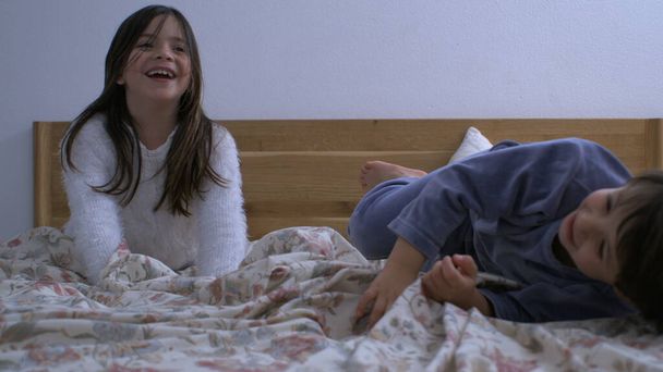 Радостный момент, когда младший брат прыгает в постель, а сестра смеется, счастливый момент семейного образа жизни, запечатленный в сверхмедленном движении со скоростью 1000 кадров в секунду - Фото, изображение