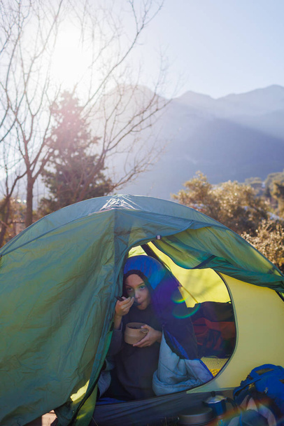 enfant prend le petit déjeuner dans les montagnes. L'enfant mange dans une tente. garçon dans un sac de couchage avec une assiette dans les mains. portrait d'un enfant dans une tente. camping et trekking avec enfants. - Photo, image
