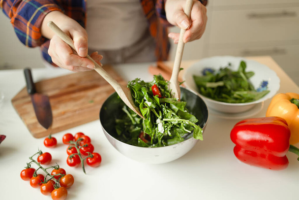 Mãos de mulher caucasiana dos anos 30 está preparando uma salada vegan saudável fresca com muitos tomates, legumes de rúcula na cozinha em casa e tentando uma nova receita. Foto de alta qualidade - Foto, Imagem