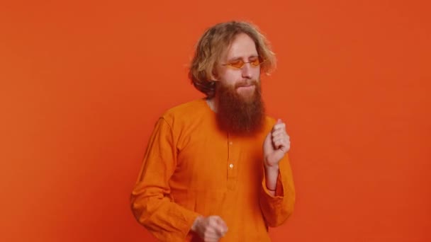 Happy smiling Caucasian man listening music and dancing disco, fooling around having fun expressive gesticulating hands relaxing on party making funny moves. Redhead guy isolated on orange background - Footage, Video