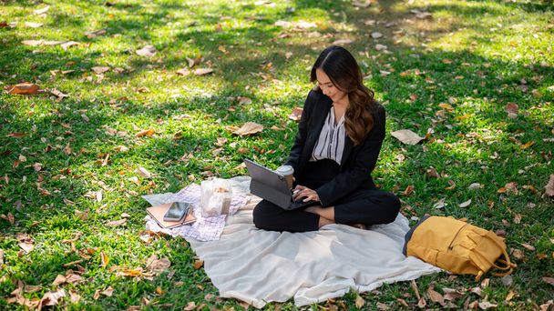 Красива азіатська бізнес-леді сіє каву і працює на своєму цифровому планшеті на пікніку в парку. - Фото, зображення
