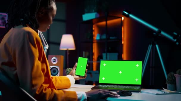 Afrikai amerikai lány használ okostelefon és PC zöld képernyőn, nézi a modern eszközök fut ugyanazt az elszigetelt mockup sablont a kijelzőn. A fiatal nő ellenőrzi a másoló képernyőket. B kamera. - Felvétel, videó