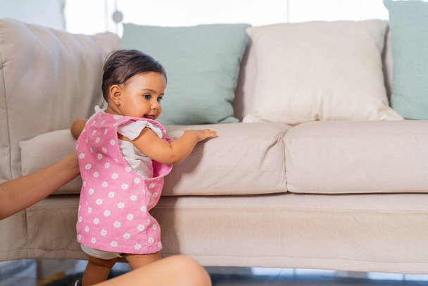 Un niño pequeño practica de pie junto al sofá en un entorno de sala de estar segura y hogareña. - Foto, imagen