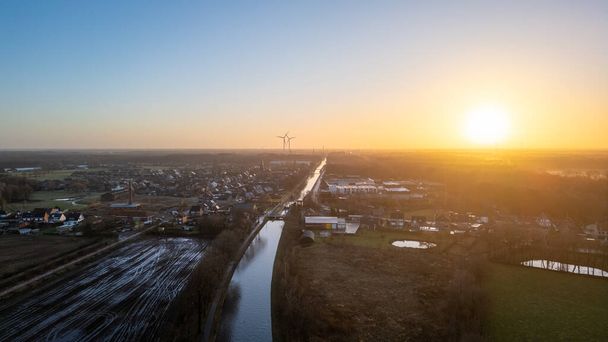 This is an aerial shot captured during sunset, casting a warm glow over a small rural town. The view encapsulates a blend of natural and man-made landscapes, with fields and buildings stretching - Photo, Image