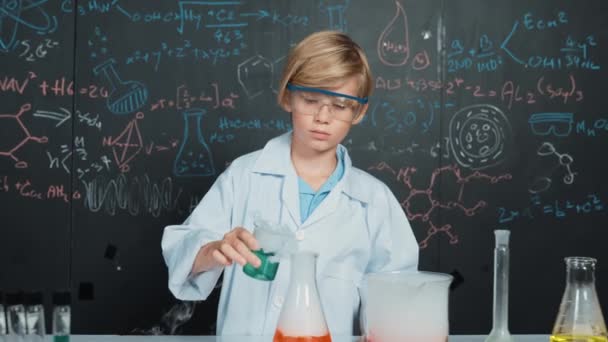 Chico inteligente inspeccionar líquido químico mixto en vasos de precipitados de laboratorio mientras sostiene y mira cuidadosamente. El niño caucásico se enfoca en hacer un experimento en la lección de química o en la clase de ciencias STEM. Erudición. - Metraje, vídeo
