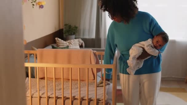 Μέτριο πλάνο της φροντίδας της νεαρής μητέρας με τον γιο βρέφος που βρίσκεται στο χέρι της προσαρμογή μαλακή κουβέρτα σε ζεστή ξύλινη κούνια του μωρού - Πλάνα, βίντεο