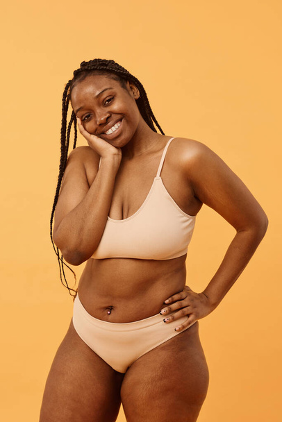 Estúdio retrato de moderna jovem afro-americana com cabelo trançado vestindo lingerie confortável posando para câmera, fundo de damasco quente - Foto, Imagem