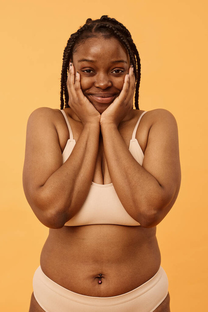 Verticaal medium portret van charmante jonge zwarte vrouw dragen comfortabele ondergoed poseren voor camera in studio - Foto, afbeelding