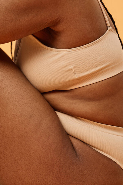 Pionowy widok z boku ujęcie nierozpoznawalny młody czarny kobieta z zakrzywionym ciała noszenie minimalistyczne bielizna siedzi w studio - Zdjęcie, obraz