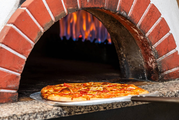 Gemengde pizza vers uit de pizza oven met vlammen zichtbaar op de achtergrond - Foto, afbeelding