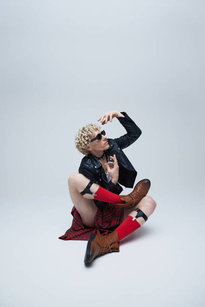 Dançarino masculino elegante combinando elementos punk e trajes escoceses em movimento espirituoso contra fundo de estúdio cinza. Conceito de fusão de moda, fotografia de arte, estilo, singularidade, auto-expressão. Anúncio - Foto, Imagem