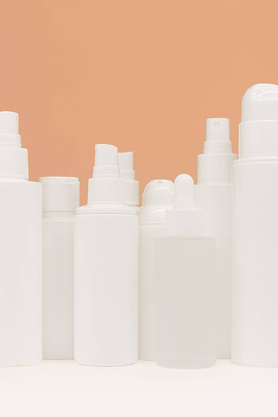 Gesichtspflegeprodukte auf weißem Tisch, Kosmetikflaschen auf Pfirsichhintergrund, Kopierraum. Eine saubere vorgefertigte Vorlage für die Markenpräsentation. Schönheitsanzeige - Foto, Bild