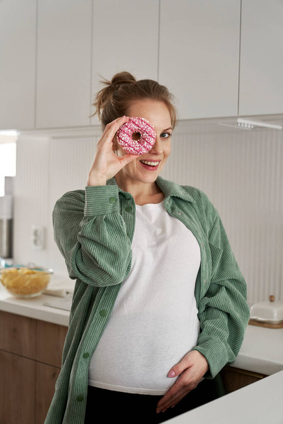 Έγκυος γυναίκα διασκεδάζει με ένα ντόνατ - Φωτογραφία, εικόνα