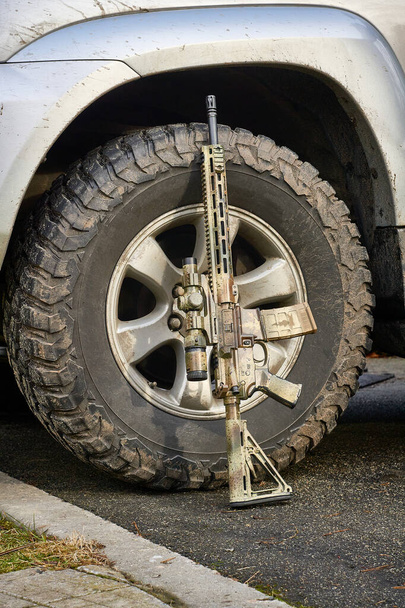 Кулемет маскувального кольору стоїть на грязьовому покритому колесі срібного позашляховика - Фото, зображення