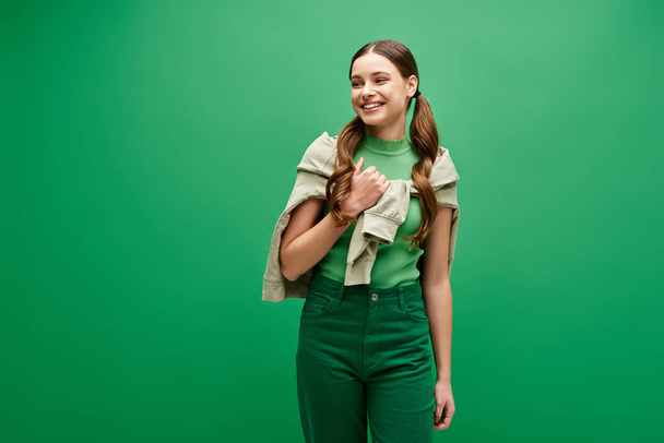 Uma jovem mulher deslumbrante em seus vinte anos de pé graciosamente contra um cenário verde vibrante em um estúdio. - Foto, Imagem