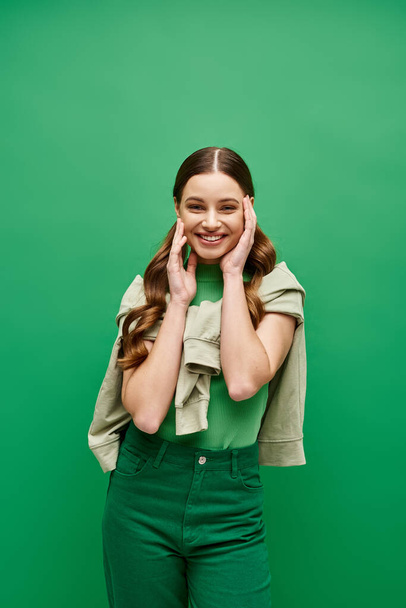 Μια κομψή νεαρή γυναίκα, γύρω στα 20, ποζάρει μπροστά σε ένα καταπράσινο φόντο σε ένα στούντιο.. - Φωτογραφία, εικόνα