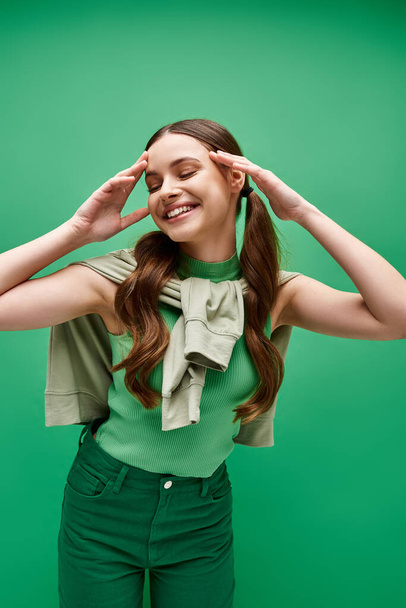 Una giovane donna felice sulla ventina con i capelli lunghi indossa una camicia verde in un ambiente da studio. - Foto, immagini
