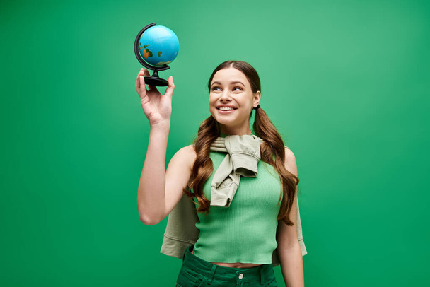 Młoda, piękna kobieta po dwudziestce delikatnie trzyma hipnotyzującą niebieską kulę w studio na zielonym. - Zdjęcie, obraz