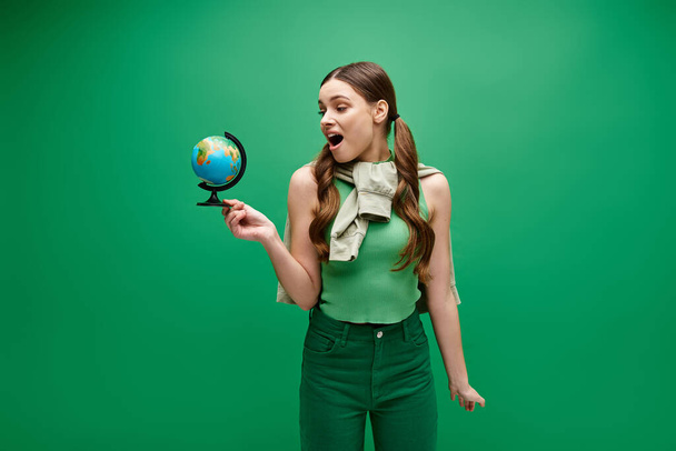 Eine junge Frau in ihren Zwanzigern hält einen kleinen Globus in der Hand, der die Verbindung und Einheit mit der Welt symbolisiert. - Foto, Bild