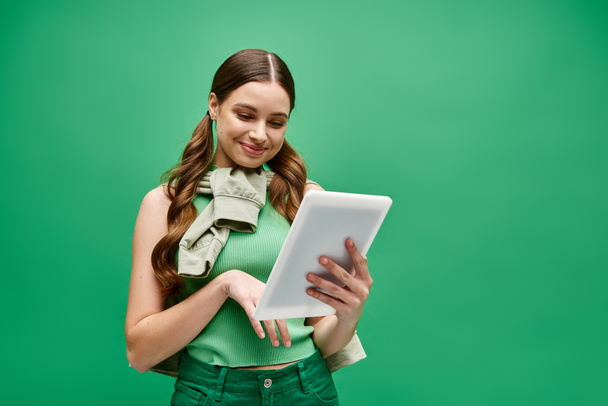 A stylish woman in her 20s, wearing a green shirt, confidently holds a tablet in a studio setting. - Photo, Image