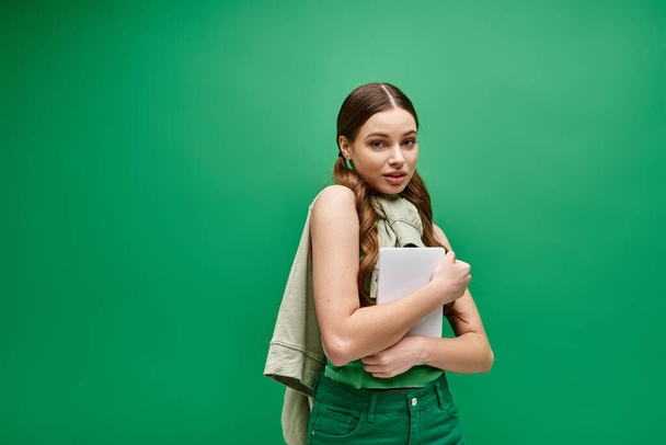 Upea nuori nainen 20-vuotiaana, pukeutunut vihreään paitaan, pitää tablettia kiehtovassa studiossa.. - Valokuva, kuva