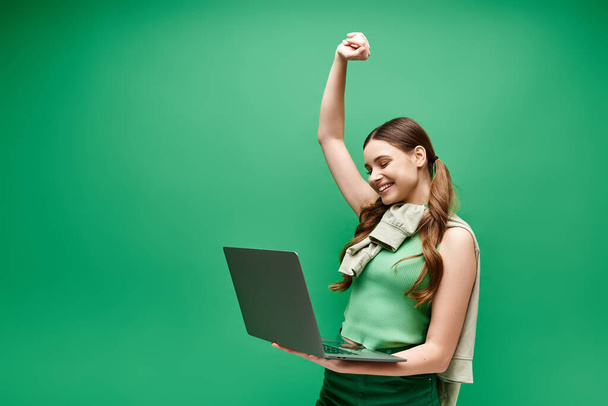 Een jonge vrouw van in de twintig, met een groen shirt aan, houdt vol vertrouwen een laptop in de studio. - Foto, afbeelding
