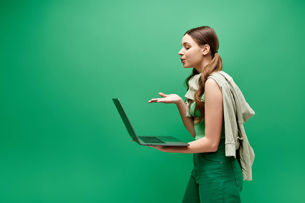Una giovane donna sulla ventina che tiene un portatile in uno studio ambientato su uno sfondo verde. - Foto, immagini