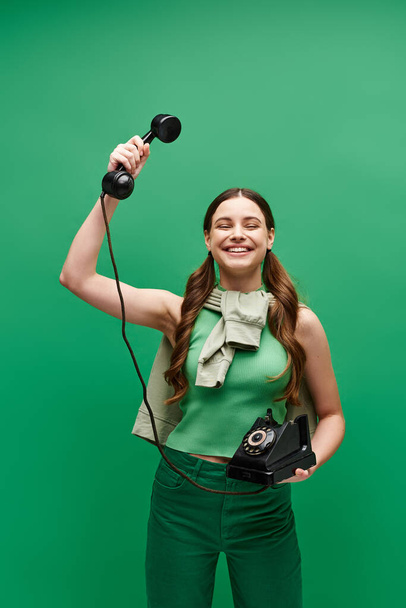 Een jong meisje in de 20 met een retro telefoon in een studio op een groene achtergrond. - Foto, afbeelding