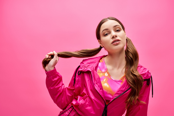 Een jonge vrouw in de 20, straalt stijl en elegantie uit, draagt een roze jasje in een studio met een levendige roze achtergrond. - Foto, afbeelding