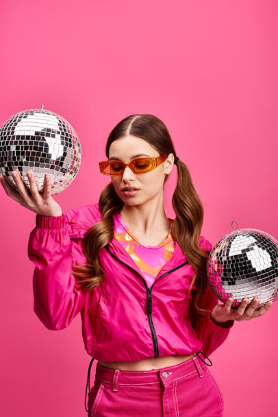 Mujer joven de 20 años sosteniendo dos bolas de discoteca frente a su cara, creando una imagen fascinante y elegante. - Foto, Imagen