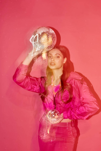 Une jeune femme élégante dans la vingtaine, portant une chemise rose, tenant une boule d'argent brillant sur un fond rose. - Photo, image