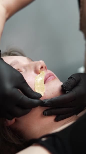 El maestro de depilación aplica cera en la cara del cliente. Remover el bigote de la mujer con cera. Primer plano - Metraje, vídeo