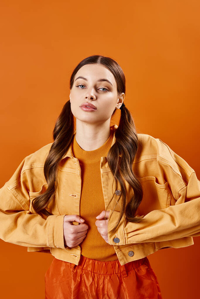 Egy 20-as éveiben járó, elegáns fiatal nő pózol egy stúdióban, élénk sárga kabátot és trendi narancssárga nadrágot visel narancssárga háttérrel.. - Fotó, kép