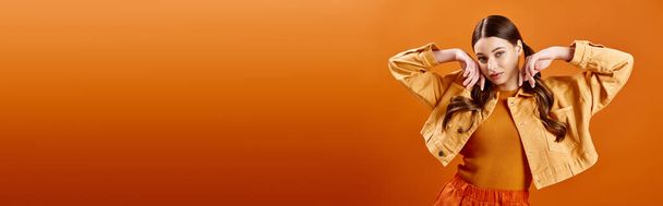 Молода жінка в 20 років в яскраво-жовтій сукні з руками на голові в студії на помаранчевому фоні. - Фото, зображення