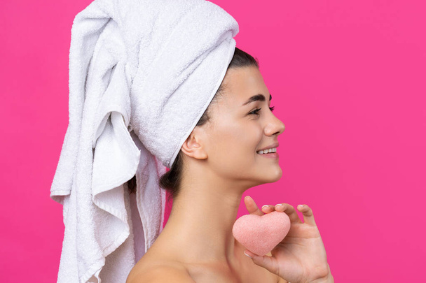 Beautiful cheerful attractive girl with a towel on her head, holds a sponge in the form of a pink heart. - Photo, Image