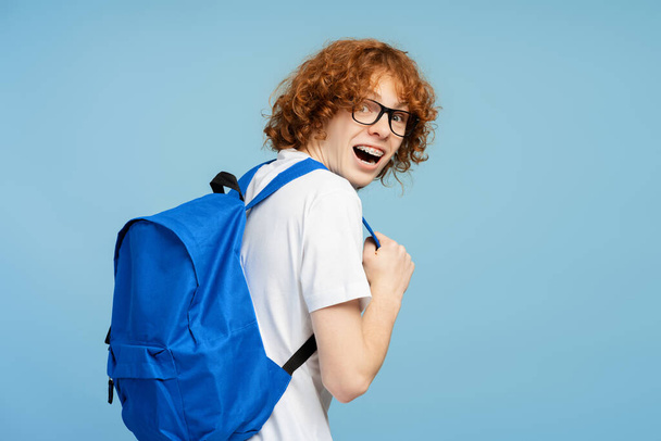 Atrakcyjna mądra studentka uniwersytetu z plecakiem patrząca na kamerę nad ramieniem, odizolowana na niebieskim tle. Koncepcja edukacji  - Zdjęcie, obraz