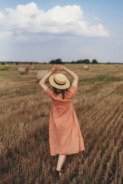 Egy gyönyörű lány hosszú ruhában és hosszú hajjal sétál a kaszált búzamezőn. A kék ég és a felhők hátterében - Fotó, kép