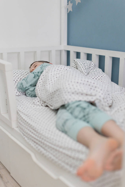 Śpiący biały chłopiec w niebieskiej piżamie w swoim łóżku - Zdjęcie, obraz