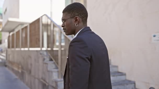 Pewny siebie dorosły czarny mężczyzna w stroju biznesowym stojący z bronią na miejskim chodniku - Materiał filmowy, wideo