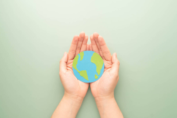 Světový den Země. Lidské ruce drží symbol glóbu na zeleném pozadí. Koncepce zelené energie, ESG, obnovitelných, udržitelných zdrojů a péče o životní prostředí. Ploché uspořádání. - Fotografie, Obrázek