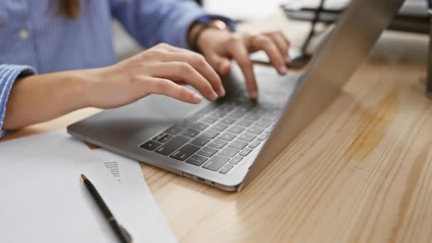 Μια επαγγελματική νεαρή γυναίκα δακτυλογραφεί επιμελώς στο laptop της σε ένα σύγχρονο περιβάλλον γραφείου, αναδεικνύοντας την παραγωγικότητα και την τεχνολογία στην εργασία. - Πλάνα, βίντεο