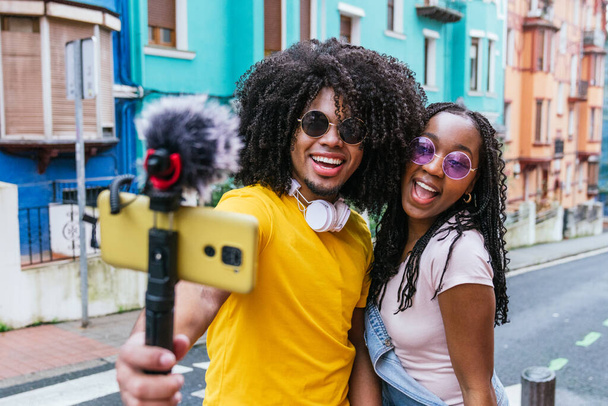 Vibrant young Latino influencers streaming live with colorful houses in the background - Photo, Image