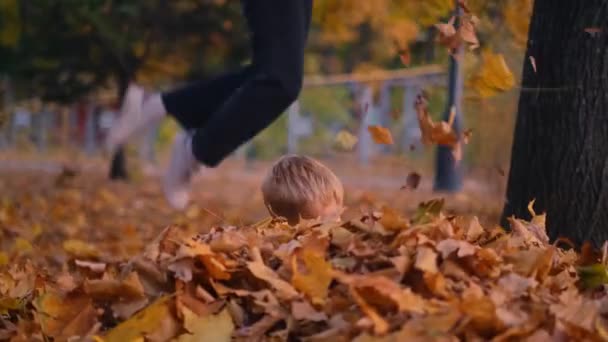 Una madre e un figlio vestiti con costumi di Halloween gettano giocosamente foglie in aria ridendo, creando una scena stravagante e gioiosa in un parco autunnale. Vivi la magia della caduta e Halloween - Filmati, video