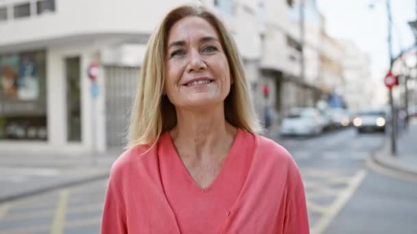 Mujer rubia sonriente con ropa casual de pie en una calle urbana soleada - Metraje, vídeo