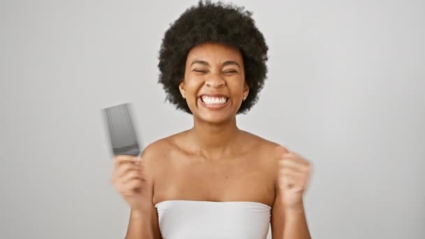 Femme afro-américaine triomphante avec les bras levés et peigne célèbre le succès, respire l'excitation et la confiance dans la serviette sur fond blanc isolé - Séquence, vidéo