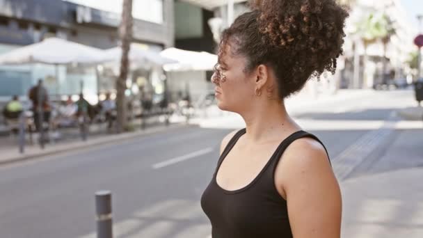 Eine junge hispanische Frau mit lockigem Haar steht nachdenklich auf einer Stadtstraße und verkörpert städtische Schönheit und Jugend. - Filmmaterial, Video