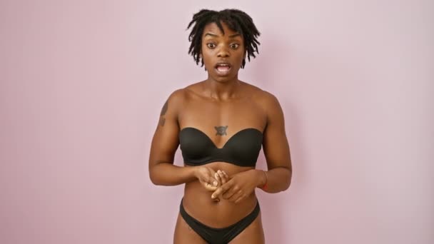 Dreadlocked young black woman in lingerie forgets, slaps forehead in 'oops' moment. over pink isolated background, memory error in crisis. - Footage, Video
