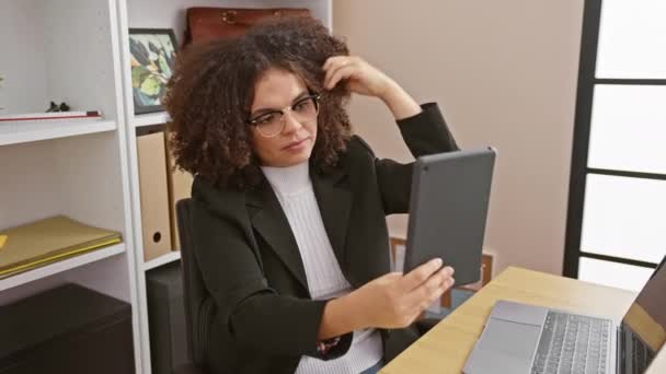 Femme hispanique aux cheveux bouclés prend un selfie dans un bureau, souriant par son ordinateur portable et sa fenêtre. - Séquence, vidéo