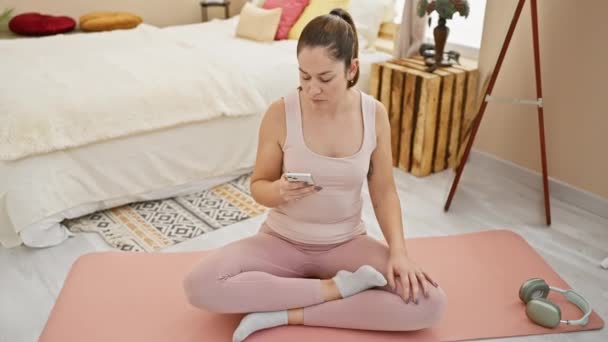 Жінка в активному одязі роздумує про рожевий килимок для йоги в затишній спальні, демонструючи свідомість і релаксацію вдома. - Кадри, відео