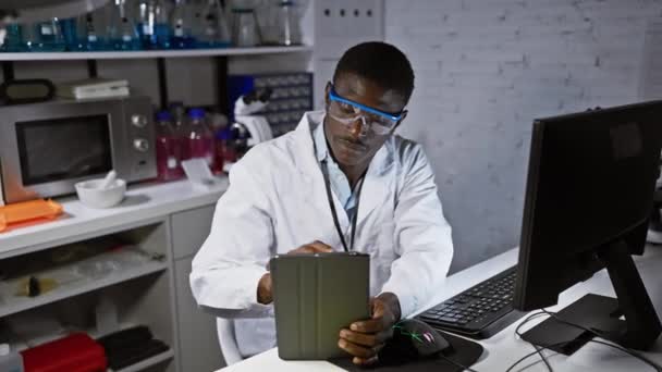 Uomo concentrato in camice da laboratorio utilizzando tablet in laboratorio, digitando sulla tastiera con attrezzature intorno. - Filmati, video